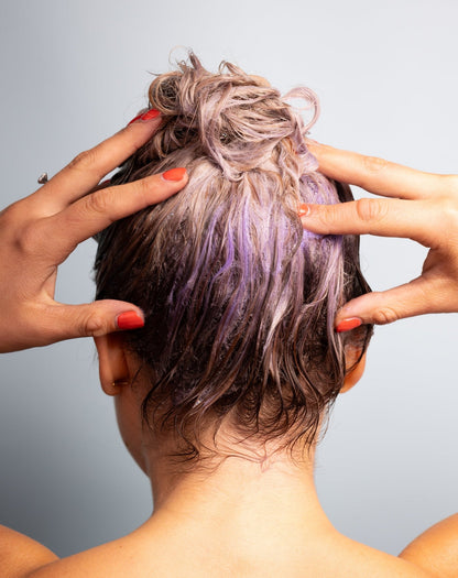 Kvinna med långt hår använder Kolai Silver burst schampo från Silver Serien, synligt reducera gula toner, bakhuvudet mot kameran på grå bakgrund